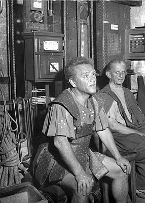 Karl Hellmer (links) wartet als Diener Sosias in Kleists "Amphitryon" auf sein Stichwort; "Schillertheater" in Berlin, August 1953; Quelle: Deutsches Bundesarchiv, Digitale Bilddatenbank, Bild B 145 Bild-F000894-0002; Fotograf: Gielow / Datierung: August 1953 / Lizenz CC-BY-SA 3.0.; Originalfoto und Beschreibung: Deutsches Bundesarchiv B 145 Bild-F000894-0002 bzw. Wikimedia Commons