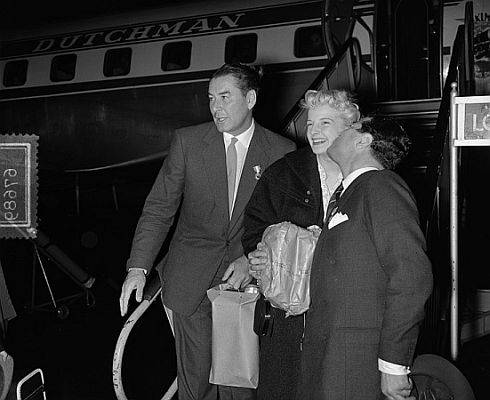 Errol Flynn (l.) mit der 17-jhrigen dnischen Schheitsknigin Krete Hoffenblad und seinem Manager Anfang Oktober 1954 am Flughafen Amsterdam Schiphol; Rechteinhaber: Nationaal Archief (Den Haag, Rijksfotoarchief; Bestandsnummer: 906-7689); Urheber/Fotograf: Wim van Rossem / Anefo; Datierung:  05.10.1954; Quelle: Wikimedia Commons; Lizenz:CC0 1.0 (Verzicht auf das Copyright)