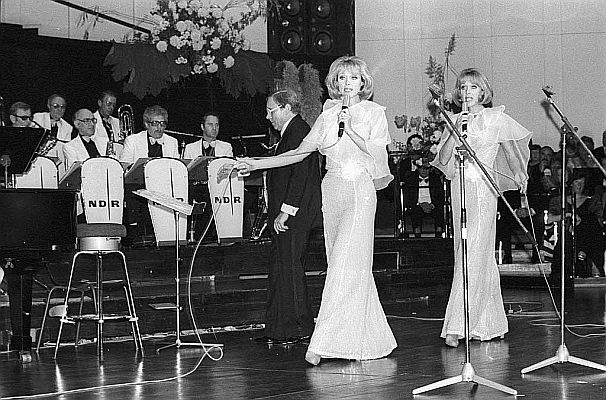 Die "Kessler-Zwillinge" am 23. Oktober 1976 mit dem Tanzorchester des "Norddeutschen Rundfunks" (NDR) unter Leitung von Franz Thon anlsslich eines Wohlttigkeitsballs des "Deutschen Roten Kreuzes" (DRK) im "Kieler Schloss"; Urheber: Friedrich Magnussen (19141987); Lizenz: CC BY-SA 3.0 DE; Rechteinhaber: "Gesellschaft für Kieler Stadtgeschichte", Bildnachlass Friedrich Magnussen (ID-Nummer: 68.396); Quelle: Wikimedia Commons von "Stadtarchiv Kiel"